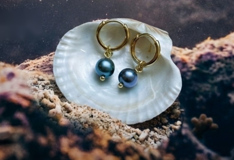 Pearl huggies by Scallop Design Co. resting in a shell on the reef, from Coral Vita’s Valentine’s Day campaign